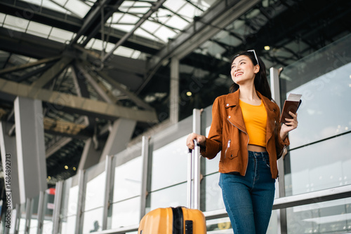 Happy young asian woman traveler using smartphone and holding boarding pass while standing at the airport terminal ready for vacation trip, smiling female tourist with confidently travel insurance