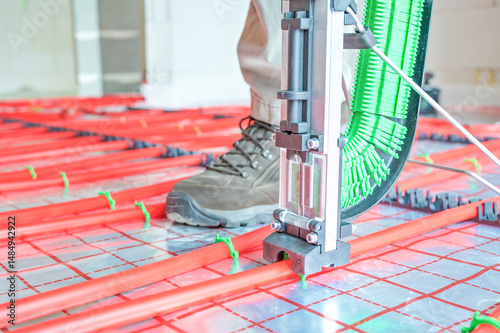 A technician skillfully installs an underfloor heating system using advanced technology, showcasing precise placement and modern plumbing techniques in a construction setting