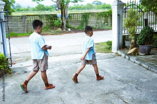 Two siblings in school uniforms walk to school.