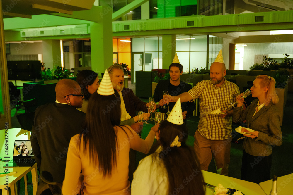 Naklejka premium Three White men, a Black man, a white-skinned woman, and two women in birthday hats are holding their glasses of champagne together while a White woman is drinking champagne and looking at them