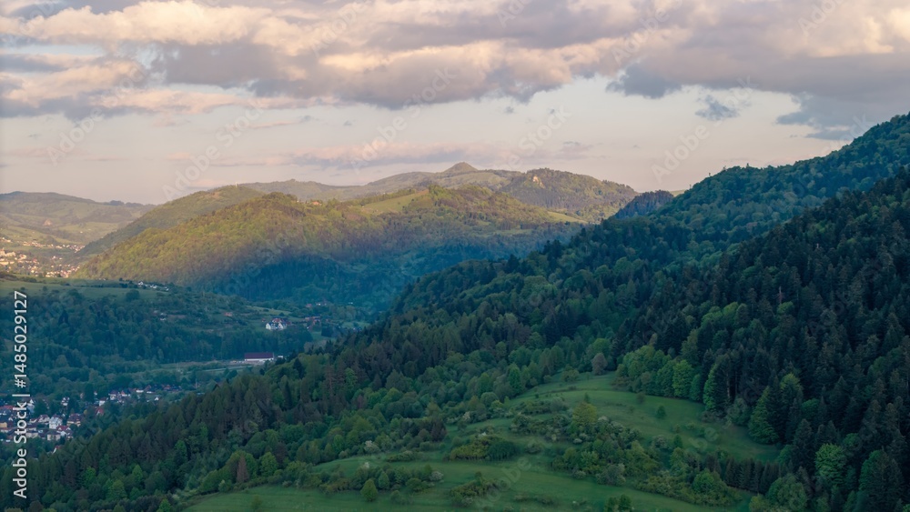 Obraz premium Aerial view of fields and landscape in the Pieniny Mountains in Poland during a May sunset, beautiful fresh spring greenery bathed in the light of the setting sun.