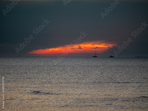 Faint sunset glow fades behind silhouettes of boats on the calm sea at Sunset Village Beach Resort, Najomtien, Chon Buri, Thailand.