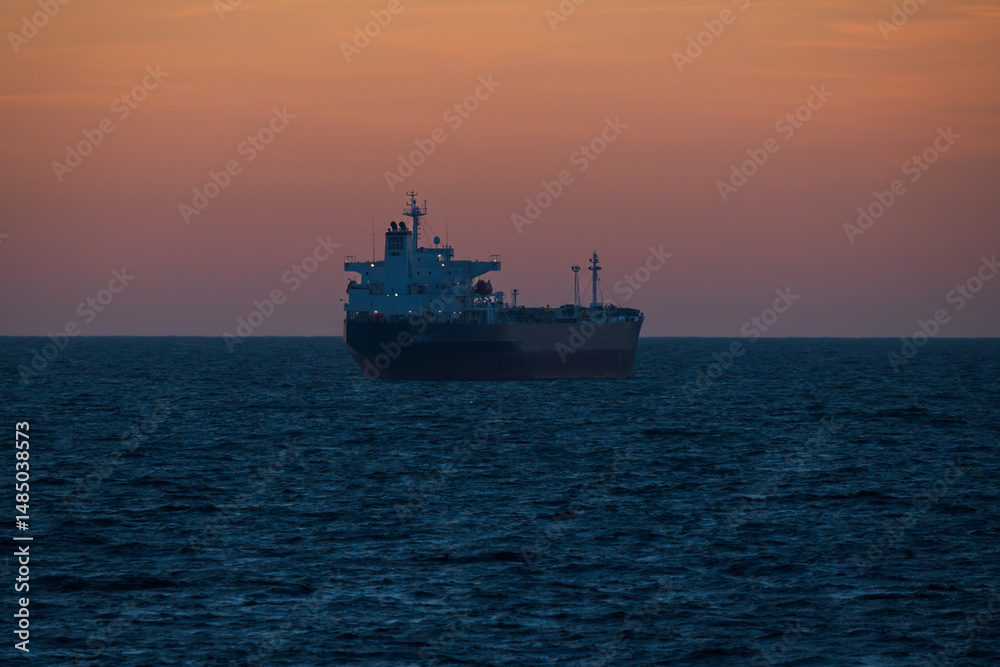 Baltic Sea: a cargo ship sails on calm waters against a picturesque sunset, reflecting the warm tones of the sky in the sea. Baltic Sea: a cargo ship sails on calm waters against a picturesque sunset, reflecting the warm tones of the sky in the sea.