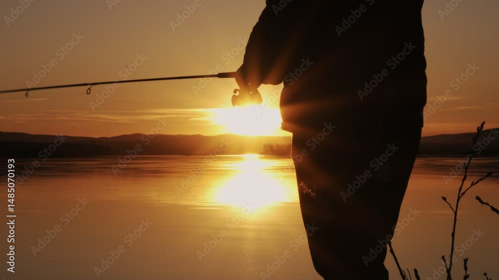 A fisherman is fishing by spinning on a lake at sunset. Close-up of a rotating fishing reel in the rays of the sun. A fishing trip.
