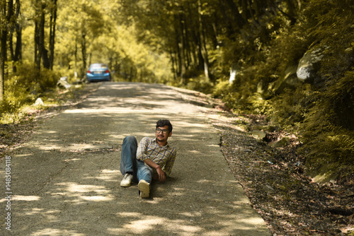 A serene forest road, sunlight filtering through trees, a man laying down peacefully on the path, embracing nature's quiet solitude