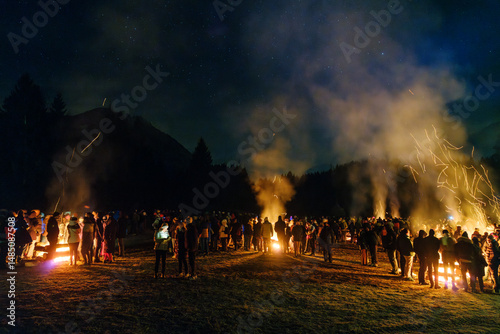 A large group of people stand around bonfires at night under a starry sky. Krampus and St Nicholas, 5 December in Tarvisio, Friuli Venezia Giulia, Julian Alps, Italy.
