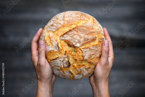 Close up of baker hands with traditional leavened sourdough bread on a rustic wooden table background. Healthy food photography