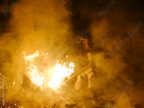 A Krampus figure stands near a bonfire, surrounded by smoke. Krampus and St Nicholas, 5 December in Tarvisio, Friuli Venezia Giulia, Julian Alps, Italy. photo