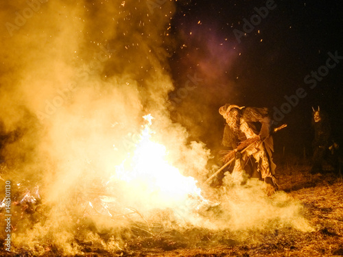 A Krampus figure stands next to a large bonfire, holding a broom. The figure has horns and a scary mask. Krampus and St Nicholas, 5 December in Tarvisio, Friuli Venezia Giulia, Julian Alps, Italy. photo