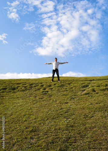 A person stands joyfully on a grassy hilltop, arms wide open, under a vibrant sky