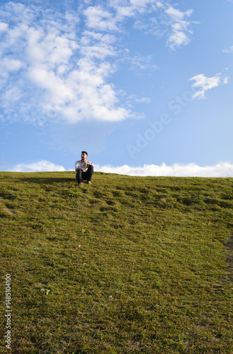 A person sits joyfully on a grassy hilltop, looking sideways, under a vibrant sky