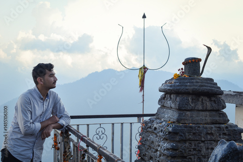 A serene moment of reflection near a Shiva temple with a mountain backdrop, trishul, and traditional offerings visible. Looking with smile at Shiva