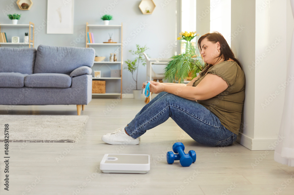 Fototapeta premium Plus-size, fat woman sad as she struggles with fitness and training, sitting on floor at home gym. Emotional challenges of weight loss, workouts, and staying motivated for wellness.