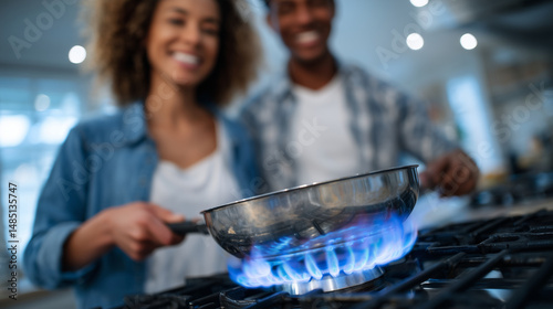 Close-up of gas stove burner with blue flames under a stainless steel pan, couple adds final touches to meal with smiles and laughter