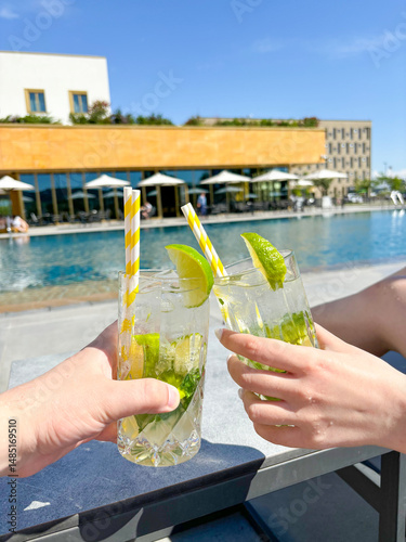 Hands holding chilled cocktails on pool background close-up, man and girl on vacation, travel and vacation concept. High quality photo
