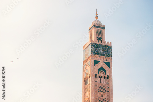 Sunlight illuminating the intricate details of the Hassan II Mosque minaret against a clear sky, showcasing Moroccan architecture