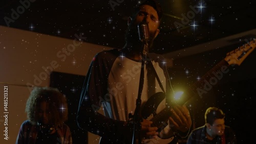 bandmates strumming guitars and singing into microphone in dim music studio, with star overlay