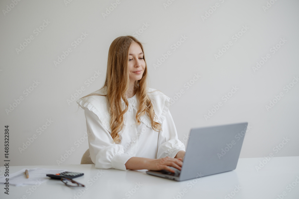Young woman working on a laptop at a minimalist desk in a bright home office during daytime Young woman working on a laptop at a minimalist desk in a bright home office during daytime
