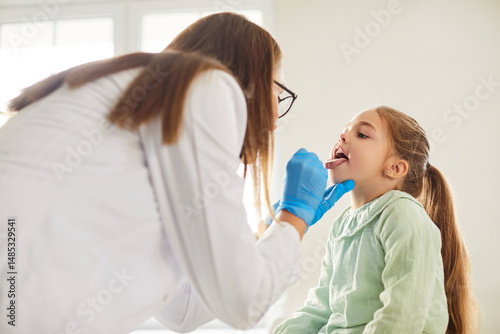 Foto Female doctor pediatrician laryngologist with tongue depressor asks little child