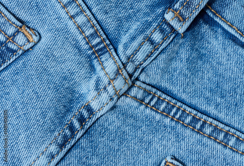 Close-up of blue denim jeans fabric showing reinforced cross-stitching. Detailed view of the seam and textile texture for design and quality themes