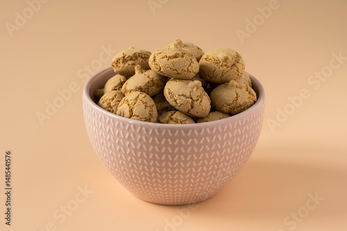 Amaretti cookie in a porcelain bowl on a beige background , side view ,high-resolution  . Delicious , crunchy biscuits for tea .