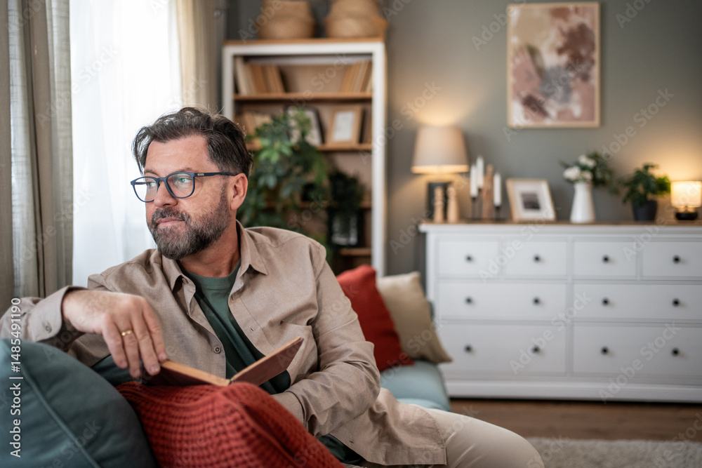 Fototapeta premium Pensive mature man pausing reading and looking out the window