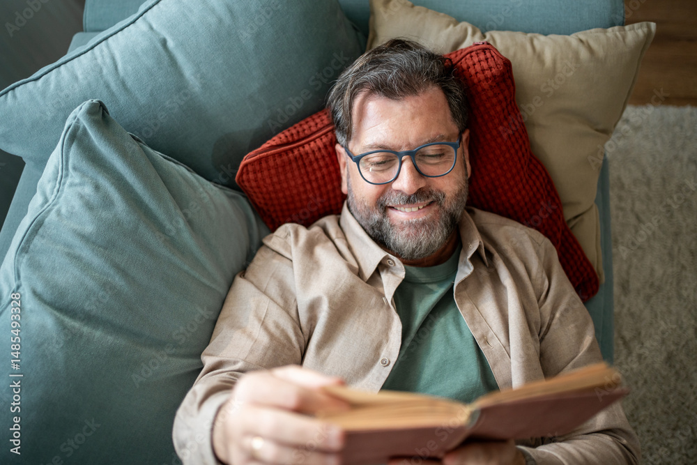 Fototapeta premium Happy senior man relaxing on sofa reading a book at home