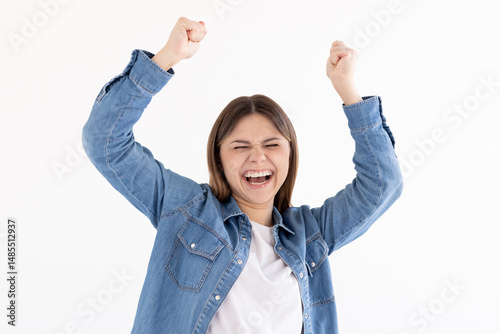 Portrait of ecstatic woman 20s wearing blue shirt clenching fist like rejoicing victory or triumph isolated over white background