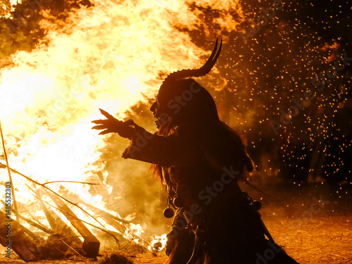 Silhouette of Krampus in a fur costume with horns, standing before a large bonfire. Krampus and St Nicholas, 5 December in mining village of Cave del Predil, Tarvisio, Italy.