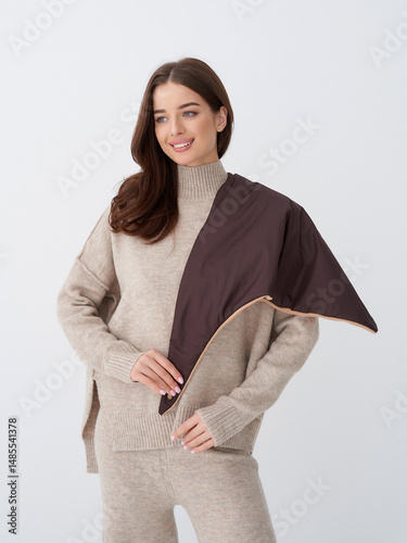Cozy scene with a smiling woman wearing a beige knit outfit. She holds a stylish brown shawl draped over her shoulder, blending elegance and warmth, conveying a sense of relaxed fashion