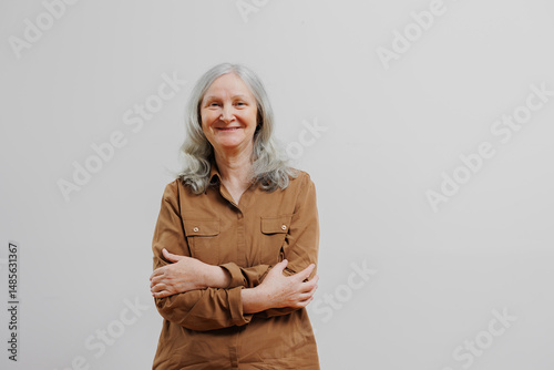Smiling elderly woman with gray hair standing against a plain background in a casual outfit and relaxed pose during daylight