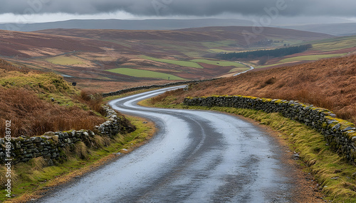 A winding rural road meanders through a hilly countryside with brown fields under an overcast sky, framed by stone walls