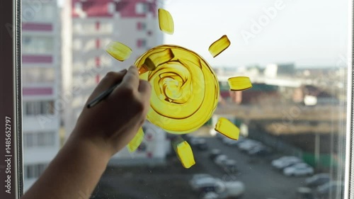 Woman's hand close up with paint brush painting sun with sun beams on the window at home. Romance, St. Valentine concept
