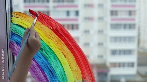 Woman's hand close up with paint brush painting colorful Rainbow on the window at home 