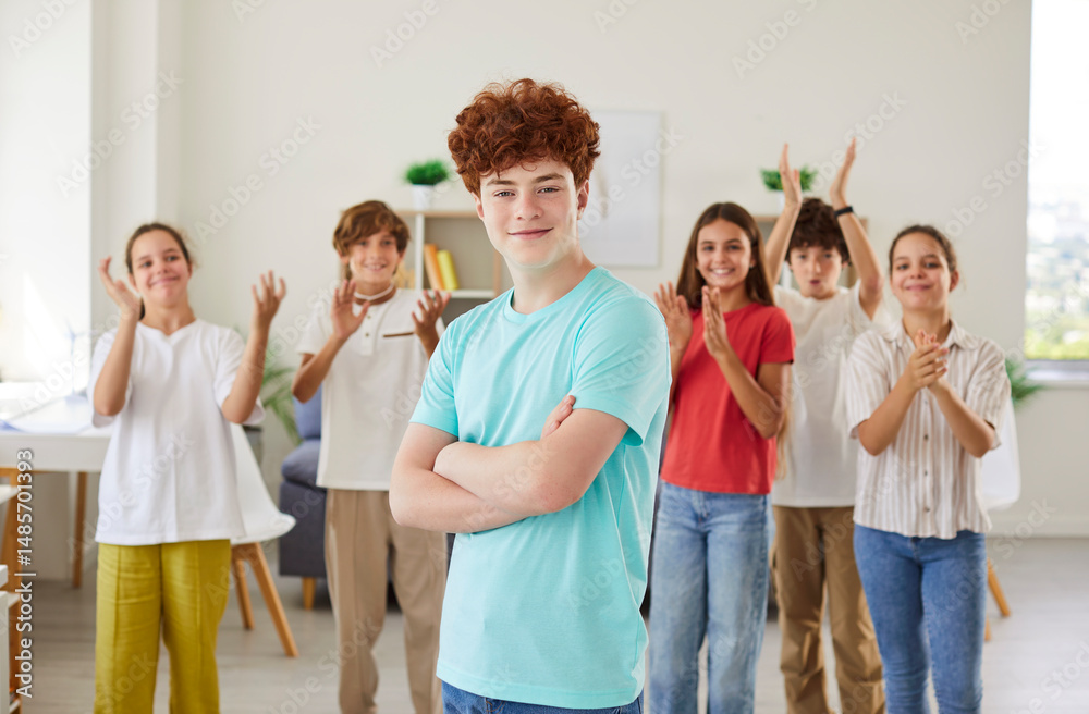 Fototapeta premium Portrait of a happy redhead schoolboy stands in front of classmates in the classroom. Joy of education and learning, highlighting the student enthusiasm for back to school experiences.