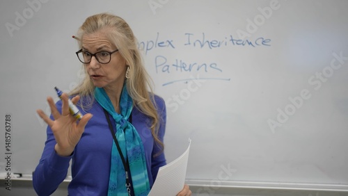 A mature female teacher writes on a whiteboard about complex biology patterns. She is engaged in teaching interacting with students in a classroom environment.