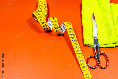 A measuring tape and sewing scissors with a yellow cloth on an orange table.