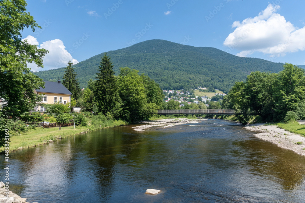 Fototapeta premium Serene river flowing gently beside lush trees and mountains under a clear blue sky on a sunny day