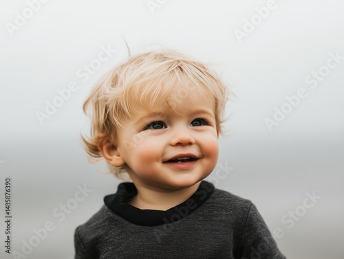 A joyful toddler with blonde hair smiling against a soft, blurred background.