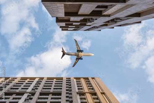 Bottom view of tall multi-story buildings against blue sky and flying passenger plane