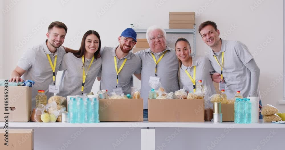 Group of happy young and mature volunteers standing in a row working together in charitable foundation preparing free food donations of foodstuffs. Volunteering concept. 4k video. Slow motion video.