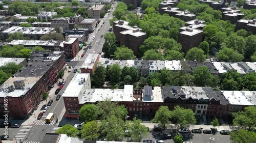 Aerial drone view of Brooklyn in spring, featuring lush green trees, classic brownstones, and quiet streets. Ideal for real estate, cityscape, and seasonal neighborhood imagery.