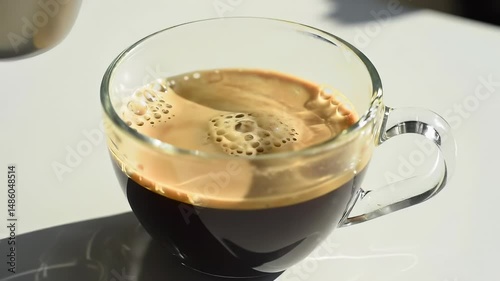 Closeup shot of fresh milk being poured into a cup of coffee, creating an appealing swirl and creamy texture. Bright, natural lighting, blending of liquids in this relaxing beverage preparation scene