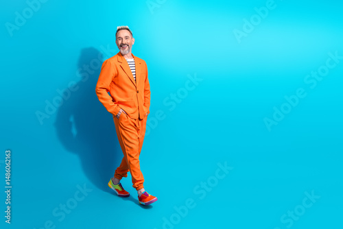 Bild auf Leinwand Confident mature gentleman in stylish orange suit posing against vibrant blue ba