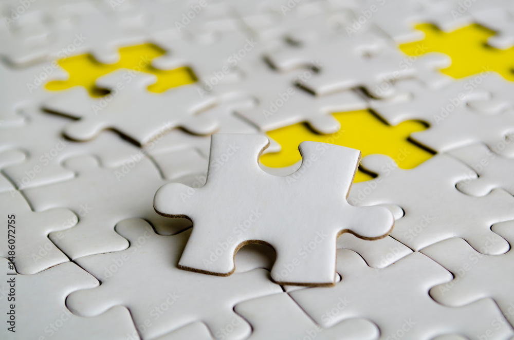 Fototapeta premium Close up of white jigsaw puzzle pieces placed on a bright yellow background with customizable space on jigsaw for text or ideas.