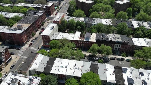 Aerial drone view of Brooklyn in spring, featuring lush green trees, classic brownstones, and quiet streets. Ideal for real estate, cityscape, and seasonal neighborhood imagery.
