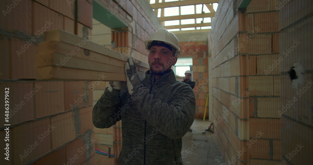 Construction worker carrying planks through corridor in house under construction, displaying focus and strength in ongoing building project Construction worker carrying planks through corridor in house under construction, displaying focus and strength in ongoing building project