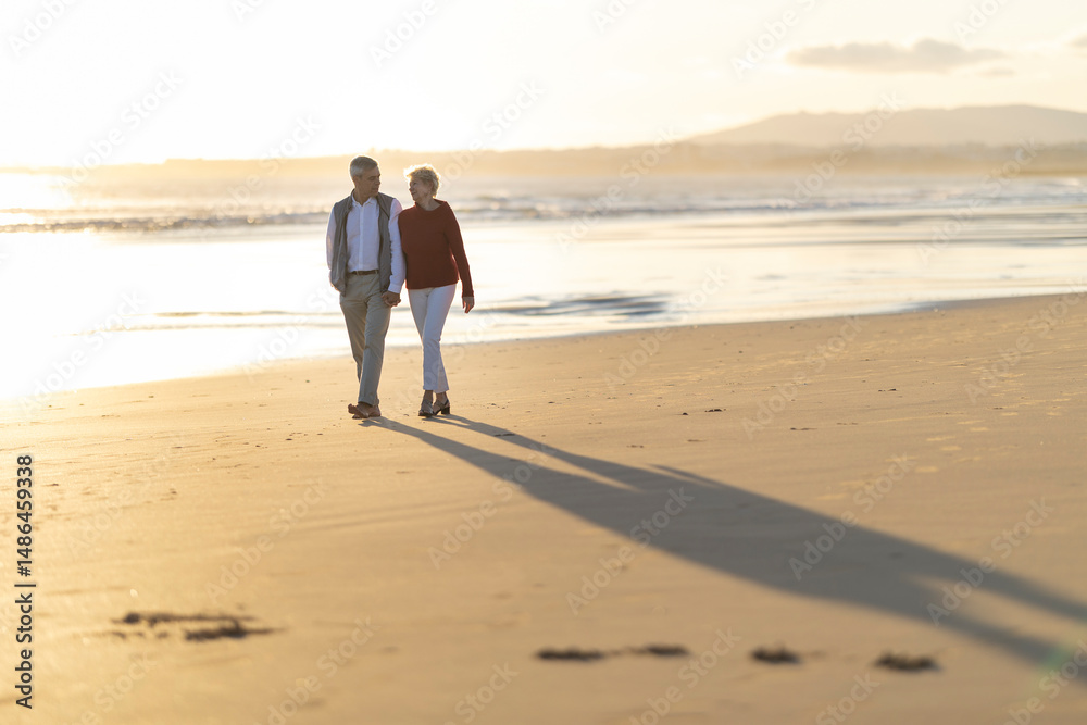 Senior couple walking on the beach at sunset holding hands Senior couple walking on the beach at sunset holding hands
