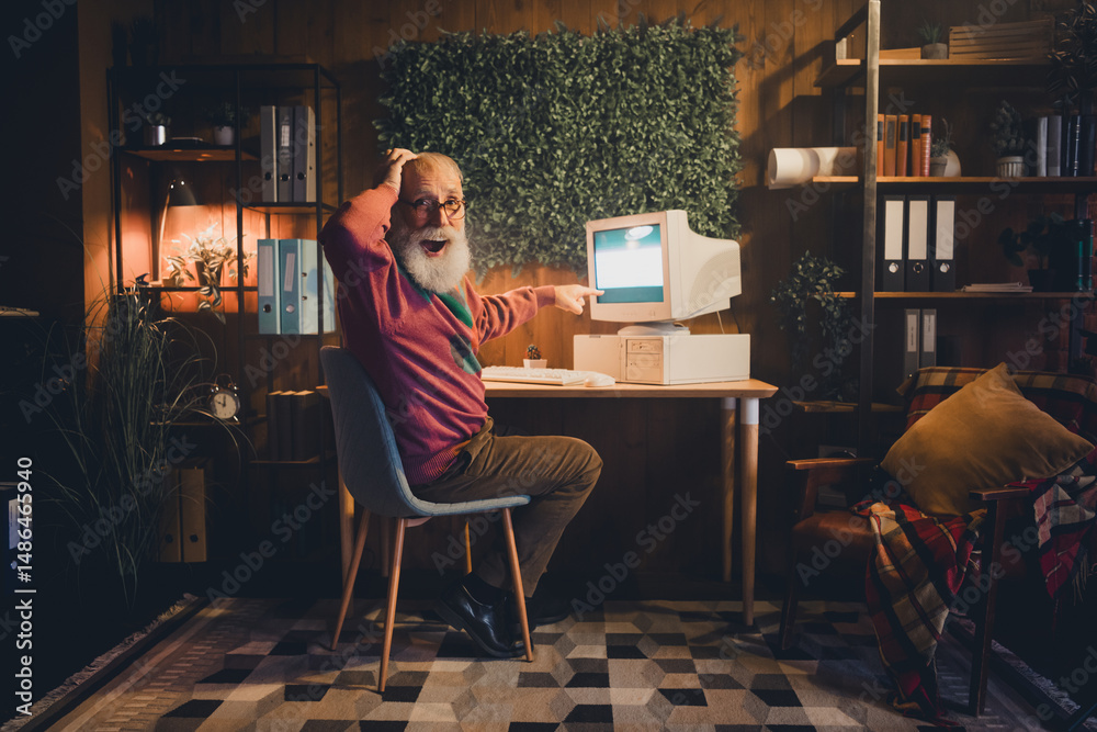 Fototapeta premium Elderly man using a vintage computer at home office, surrounded by books and learning materials, symbolizing technology and remote working