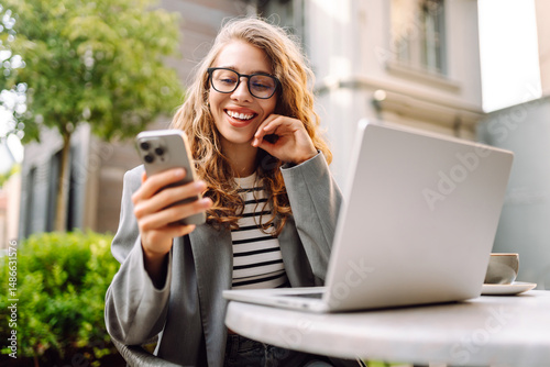 Wallpaper Mural Woman in glasses works with a laptop on a summer terrace of a cafe with a phone in her hands. Female freelancer with phone and laptop enjoys the sunny weather. Freelancing, technology concept. Torontodigital.ca